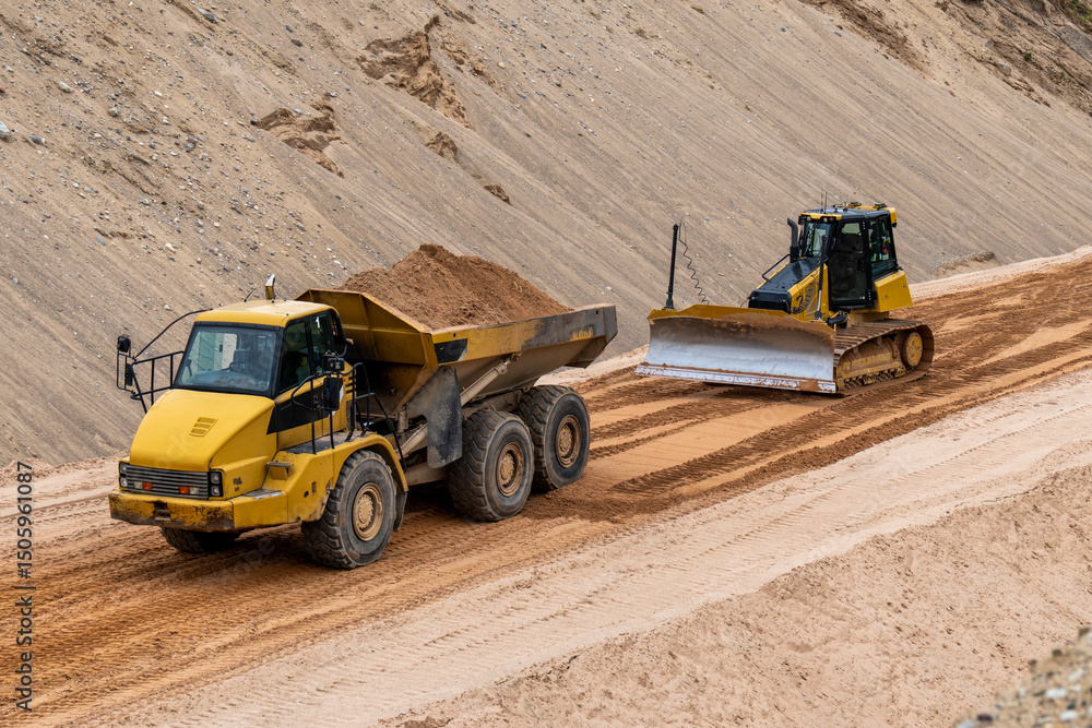 Heavy construction vehicles working on sandy site, dump truck and bulldozer leveling ground at quarry or infrastructure construction zone Heavy construction vehicles working on sandy site, dump truck and bulldozer leveling ground at quarry or infrastructure construction zone