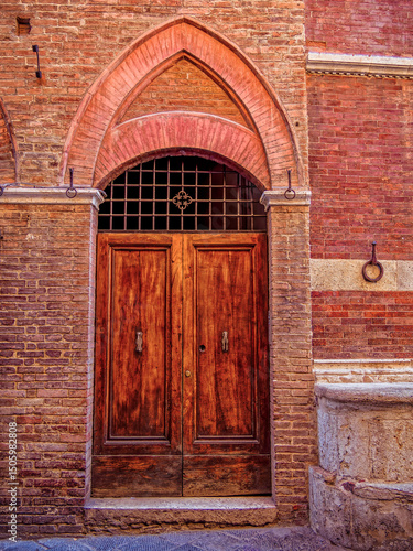 Wallpaper Mural Elegant wooden door within a carved stone archway. The intricate details and textures highlight the region’s architectural charm. Travel to in Siena, Tuscany, Italy. Torontodigital.ca