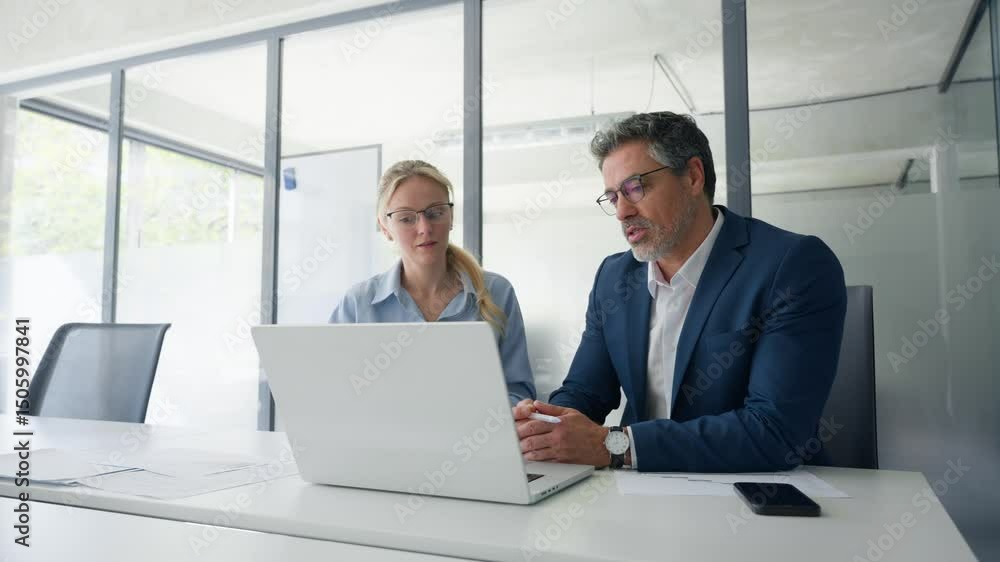 Two partners, team of professional business people working, discussing work sitting at desk. Mature focused senior mentor leader man showing young woman manager project on laptop in office. Copy space