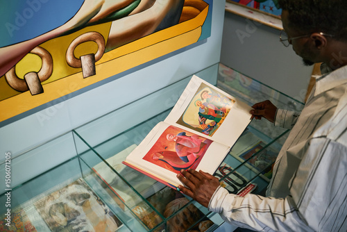 Tableau sur toile Person exploring modern art exhibit while holding catalog and reviewing vibrant artworks displayed in the showcase
