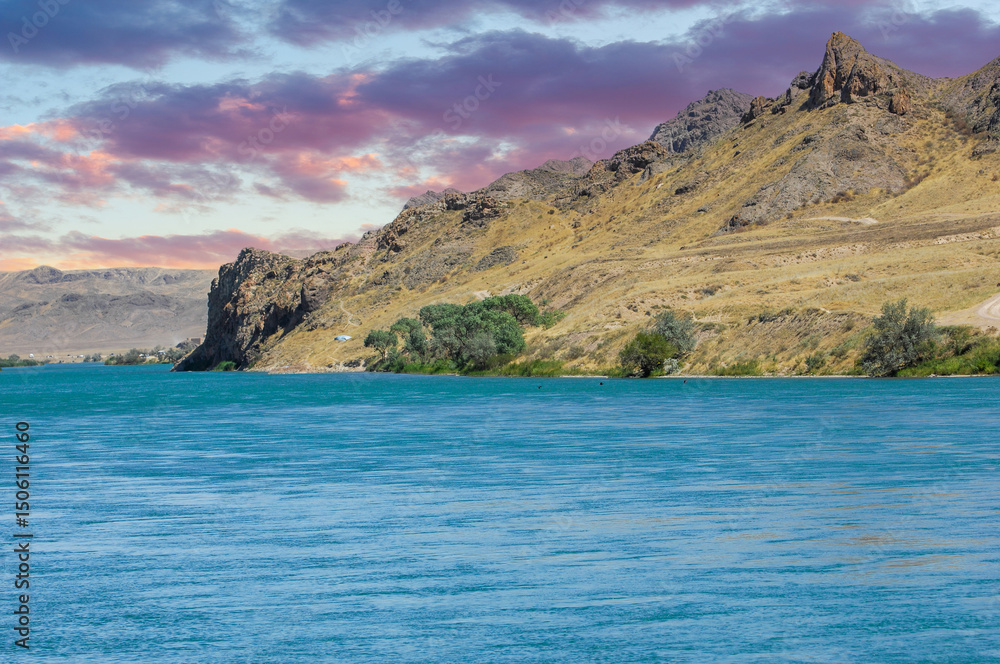 Naklejka premium Enjoy the beauty of nature in all its glory. Watch the sun set over the calm river. Enjoy the majestic mountains and lush green trees surrounding you.