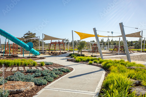 A well-designed public playground in suburban Australia, featuring large shade sails, and landscaped garden beds. Urban park design of public recreational facilities in a residential neighborhood
