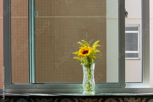 glass jar with a sunflower flower in the morning sunlight in apartment window overlooking another building