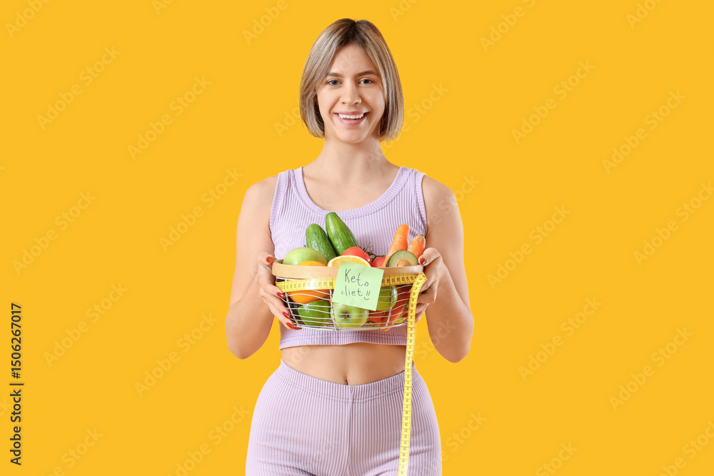 Sporty young woman holding basket with text KETO DIET and food on yellow background Sporty young woman holding basket with text KETO DIET and food on yellow background