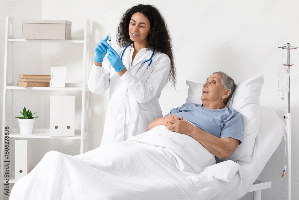 Fototapeta premium Female African-American doctor giving injection to senior patient in hospital room