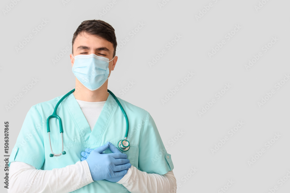 Male nurse in medical mask keeping his hands on heart against light background Male nurse in medical mask keeping his hands on heart against light background