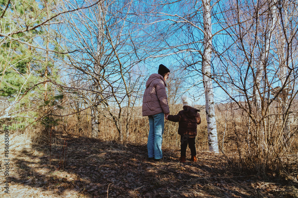 Fototapeta premium A mother and her 3-year-old daughter walk together in the park, enjoying nature and quality family time. A heartwarming moment of love, care, and happiness as they explore the outdoors together