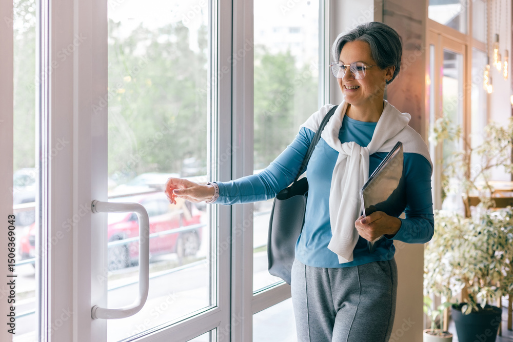 Happy senior woman with laptop leaving cafe, opening glass door with smile, confident and relaxed Happy senior woman with laptop leaving cafe, opening glass door with smile, confident and relaxed