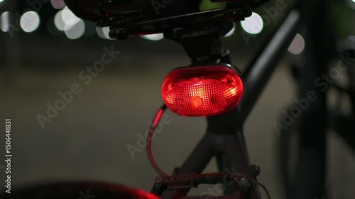 Pan camera movement around a back side of a bicycle with a blinking red light at night. Selective focus, nice blurry background.