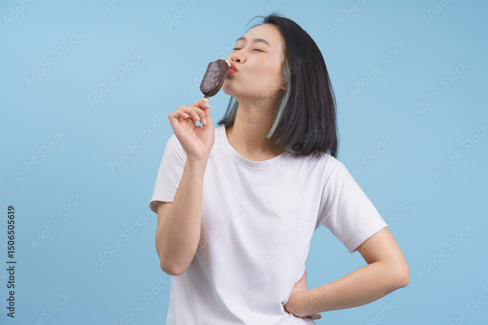 Young woman enjoying a chocolate ice cream treat against a blue background during a sunny day Young woman enjoying a chocolate ice cream treat against a blue background during a sunny day