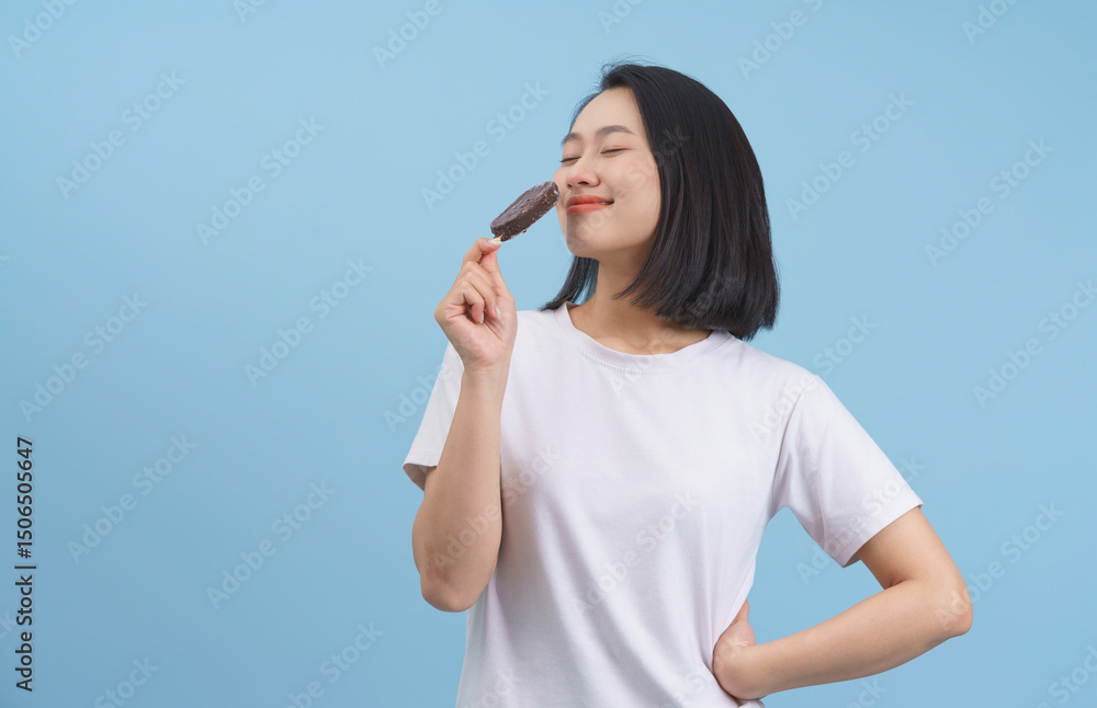 Smiling young woman enjoying chocolate ice cream against a blue background in a playful indoor setting Smiling young woman enjoying chocolate ice cream against a blue background in a playful indoor setting