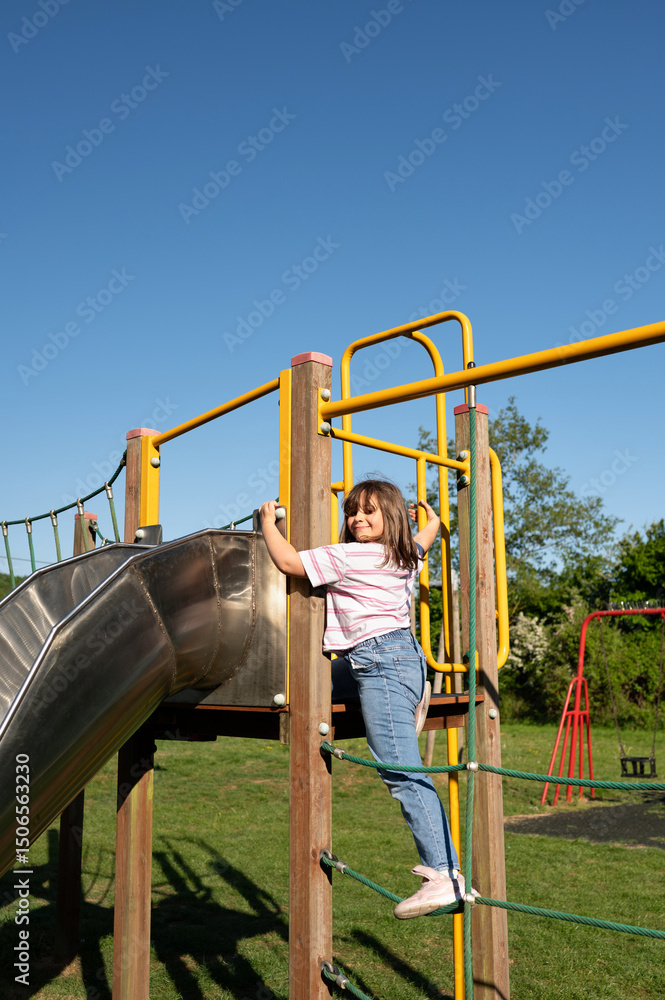 Fototapeta premium Smiling child climbing to slide. Hanging on the vertical bar.