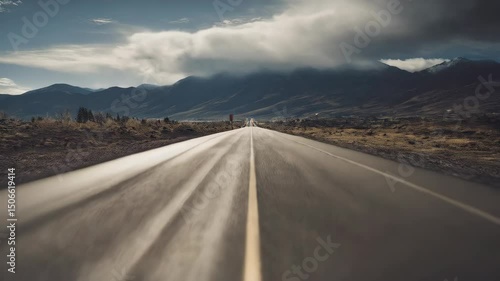 Perspective of a desolate asphalt road with a center line leading toward hazy mountains under a cloudy sky, creating a lonely yet adventurous mood.