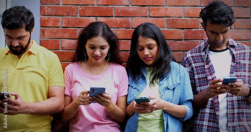 College students busy using smartphone outdoors, Indian Asian university classmates sitting on stairs or standing against wall in campus while scrolling, texting or surfing social media on mobile