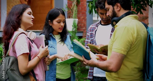 Standing students discussing project outdoors as Indian university classmates have a chat with laptop, book, and notes in college campus garden, sharing ideas and fruitful conversation together