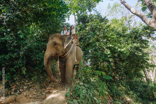 Photography Two people ride an elephant through a lush jungle, accompanied by a local guide