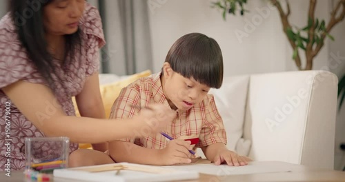 Asian Mother and young son with Down syndrome painting and drawing together on a sofa in the living room. Bonding moment of love, learning, support, and inclusive family education.