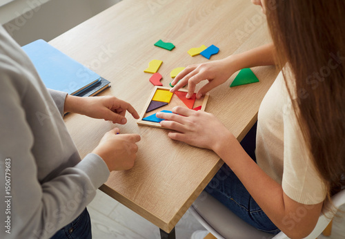 Tableau sur toile Closeup top view of children hands collecting wooden colorful geometric figures sitting at table at home