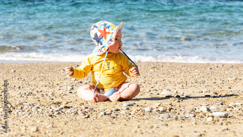 Happy baby with sun hat and UV protection enjoying at the beach