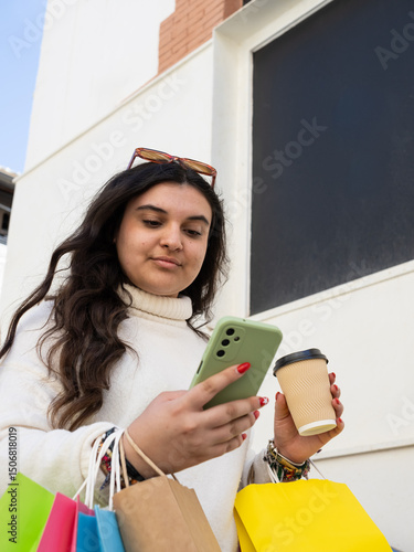 Young woman using smartphone and holding coffee after shopping