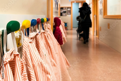 Tablou pe pânză Striped smocks hanging on colorful hooks in a nursery school hallway