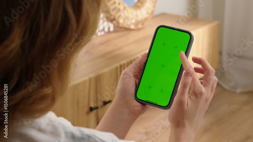 Woman sit use digital tech cell phone with green screen mock up. Hand scroll phone web site, swipe like photos. Girl hold mobile closeup. Chroma key page. Cozy home background. Online app copy space.
