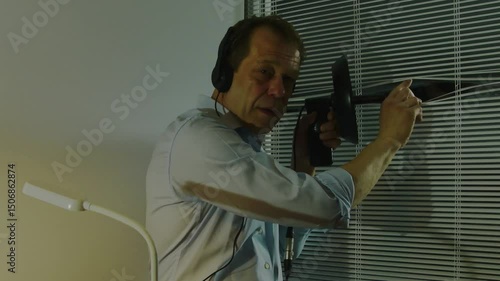 A man wearing headphones conducts covert surveillance through blinds using a directional microphone. The concept of espionage and covert investigation.