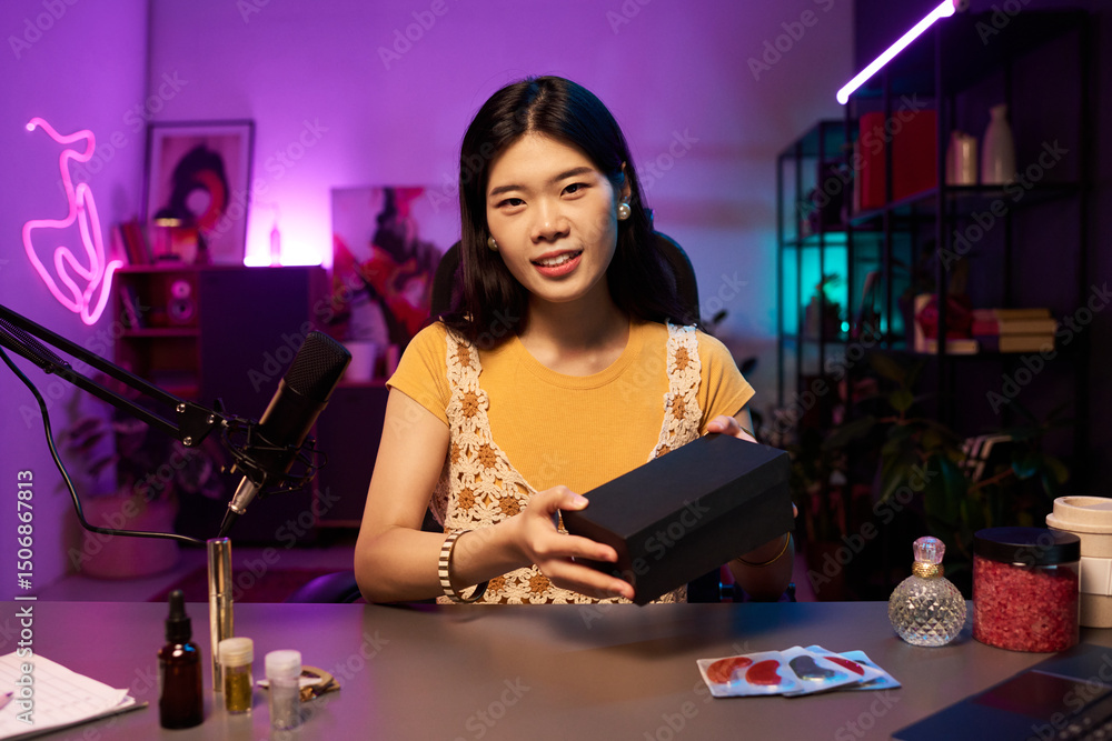 custom made wallpaper toronto digitalWoman smiling while holding a black beauty box during promotional livestream on social media. Neon lights and decor creating a cozy creative atmosphere