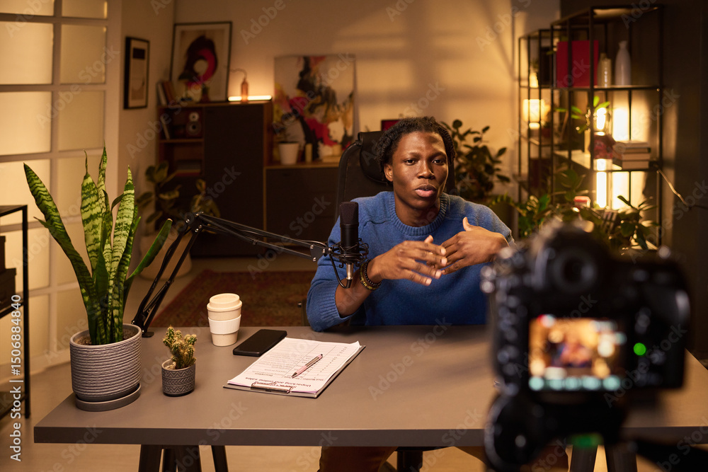 custom made wallpaper toronto digitalBlack man with dreadlocks sitting at desk with microphone, recording podcast episode in modern home studio environment. Background includes plants and bookshelves
