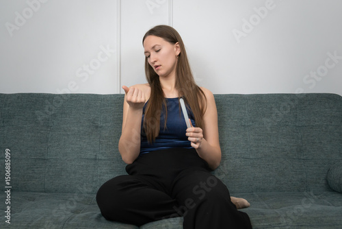 Concentrated young woman filing her nails with glass nail file while sitting comfortably on a sofa in her living room, enjoying a moment of self-care and beauty routine Free Download Concentrated young woman filing her nails with glass nail file while sitting comfortably on a sofa in her living room, enjoying a moment of self-care and beauty routine - GFXLoad