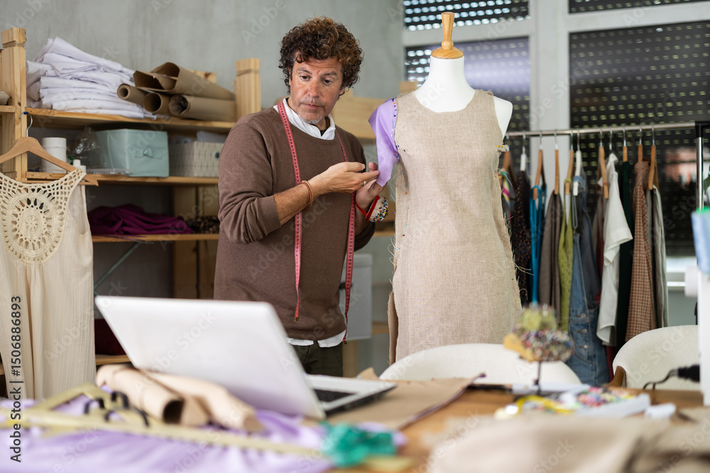 Fototapeta premium Man seamstress communicates with customer via video call work with mannequin. Contractor clarifies details with customer, discusses work issues using laptop device and remote technology.