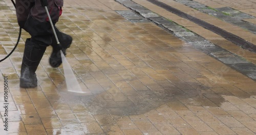 Municipal cleaner is cleaning the pavement tiles with a pressure washer on the street
