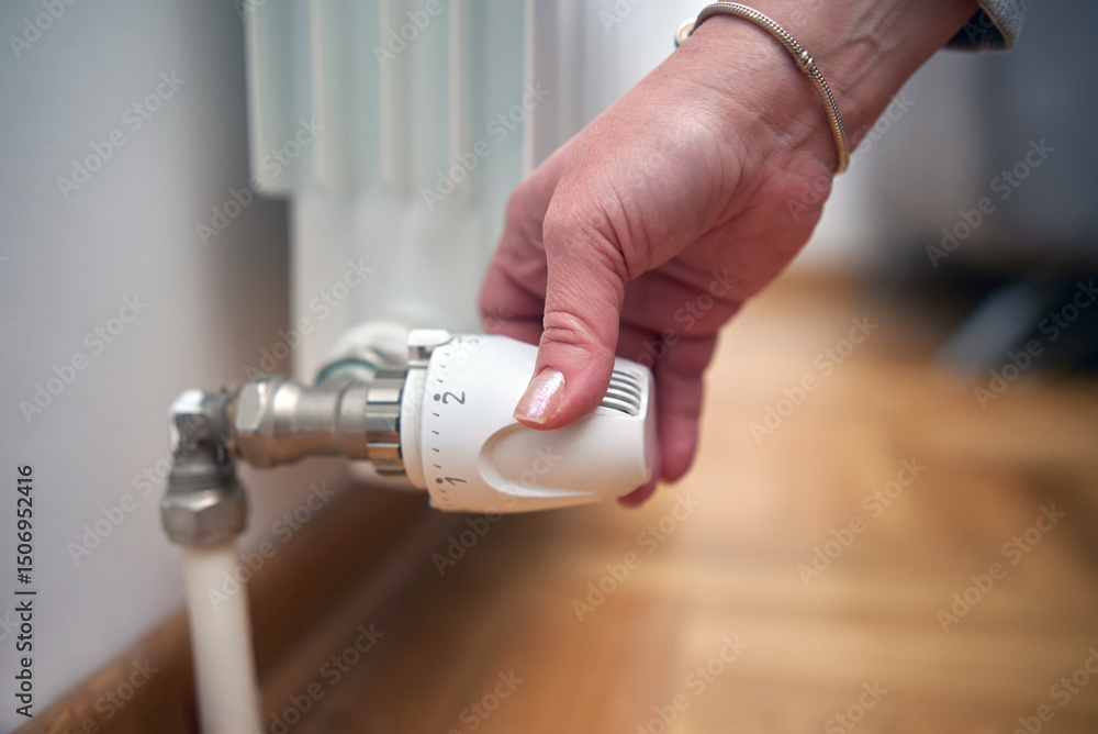 Naklejka premium Woman rotating heating valve on a chilly winter day, energy and gas crisis, cold room, heating problems.