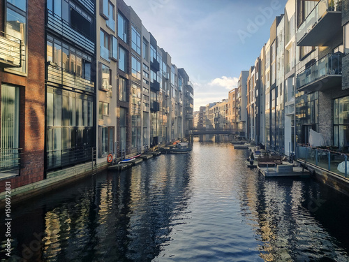Copenhagen - Modern residential buildings line a calm canal in Sluseholmen, Copenhagen, Denmark. The contemporary architecture is reflected in the water under a clear sky, showcasing urban living.
