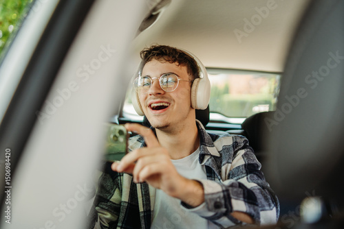 Young man taking photos with smartphone from the backseat of the car
