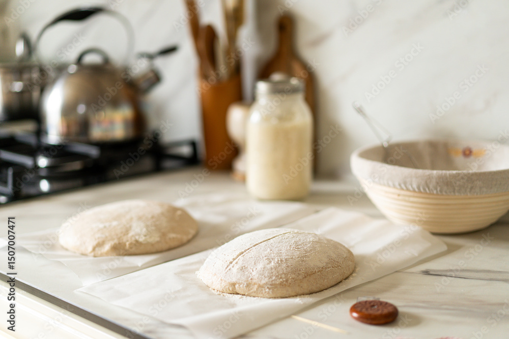 Fototapeta premium Freshly prepared sourdough bread dough rests on parchment near a container of active starter and a mixing bowl, showcasing the art of home baking.