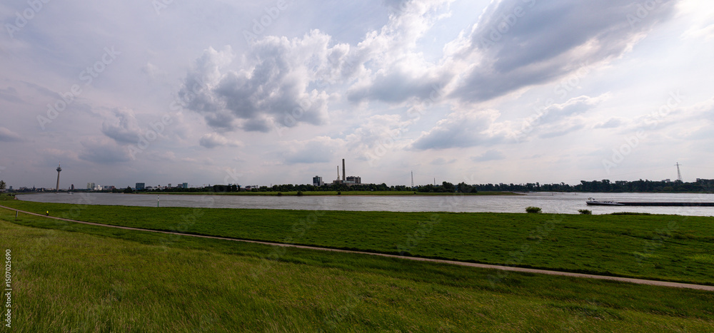 Fototapeta premium Grass field, Rhine river and Dusseldorf in the distance with cloudy sky