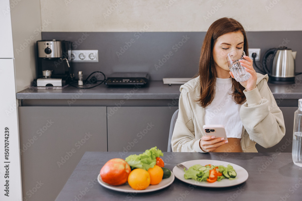Young woman drinking water and using smartphone in kitchen Young woman drinking water and using smartphone in kitchen
