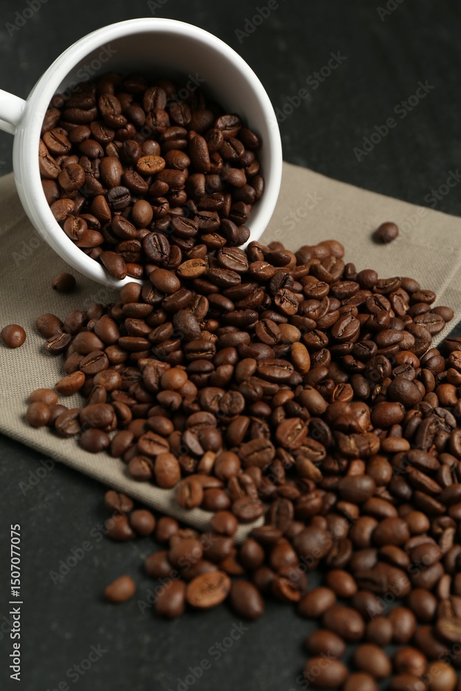 Fototapeta premium Aromatic coffee beans and overturned cup on black table, closeup