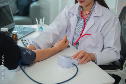 Female doctor gives advice and explains to patient for annual health check in examination room by measuring blood pressure and taking basic history. Health care and medicine concept.