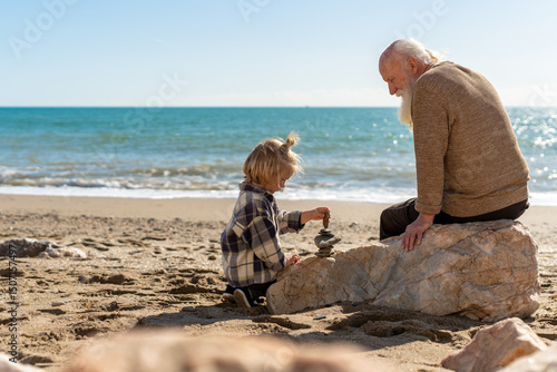 Grandfather and grandson building a stone tower together on the beach