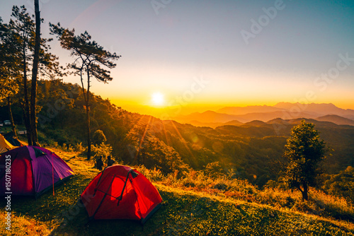 Wide angle view of two tents in the morning. The sun rises behind Doi Luang Chiang Dao mountain in Chiang Mai, Thailand. There are many tree around in the forest. Idea for camping background.