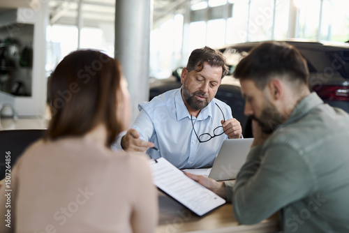 Fototapeta Car salesman explaining the contracts to a couple during a meeting at a car dealership