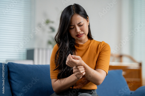 Tableau sur toile Asian woman massaging her painful wrist at home, suffering from arthritis, carpa