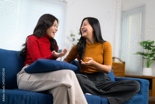 Two friends are sharing a lighthearted moment, engaging in conversation and laughter while relaxing on a sofa in a cozy living room