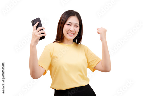 Asian young beautiful smiling woman in a yellow shirt holds a smartphone and raises her fist in a celebratory gesture.