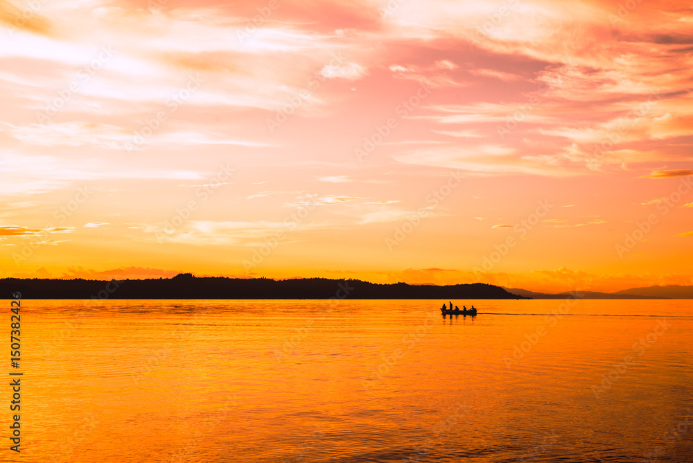 Naklejka premium Sunset on the beach with the silhouette of mountains and fishermen with their boats at sea