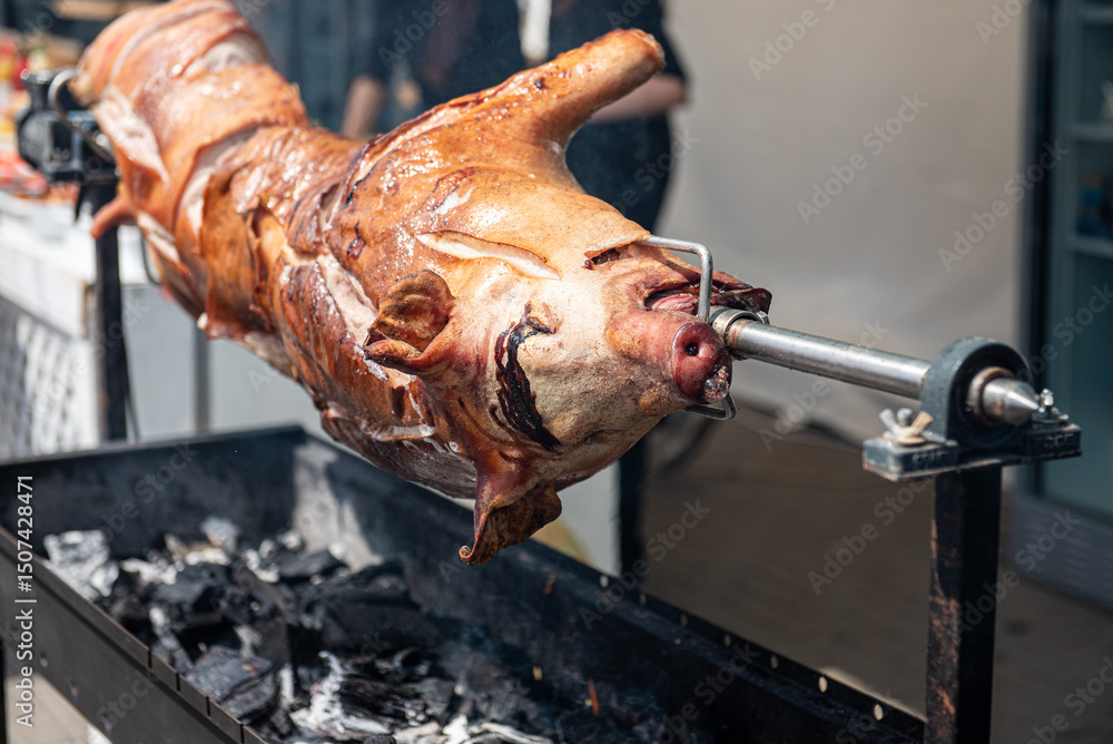 Whole suckling pig roasting on spit at outdoor street festival