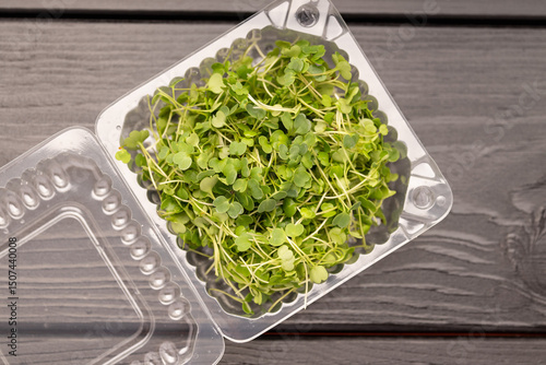Top-down view of green microgreens in a clear container on a wooden surface.