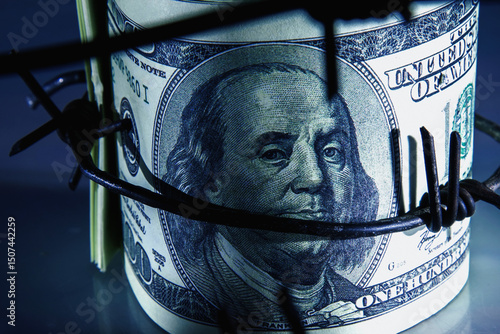 Economic warfare, sanctions and embargo busting concept. Top view of US Dollar bills money wrapped in barbed wire. Macro image.